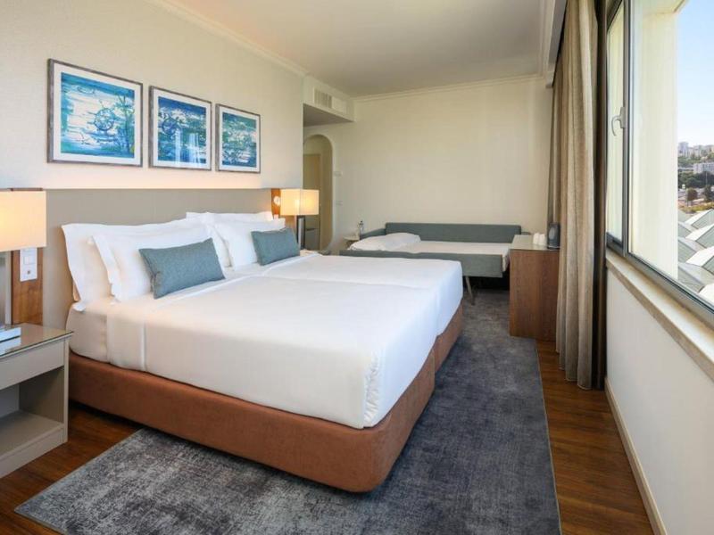 Camera d'hotel moderna con letto grande, panca, tappeto e vista sulla città.