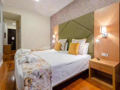 Pohodlný dvoulůžkový pokoj s dřevěnou podlahou, moderním čelem postele a teplými nástěnnými lampami.