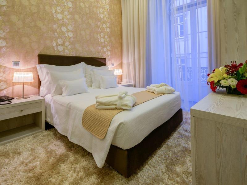 Camera d'hotel accogliente con letto matrimoniale, comodini, lampade e composizione floreale.