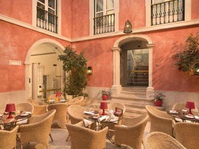 Hotelové nádvoří s červenými stěnami, stoly a židlemi za přirozeného světla.