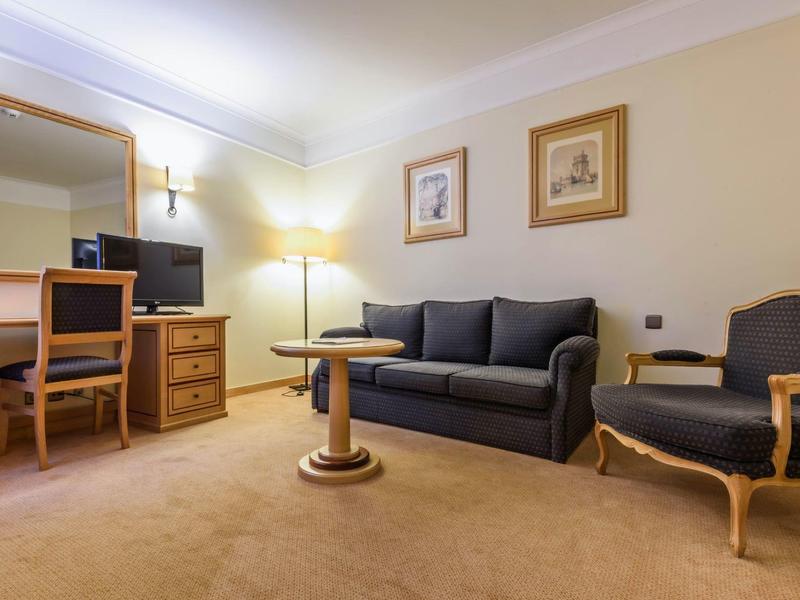 Accogliente lounge dell'hotel con divano, poltrona, scrivania, specchio e moquette morbida.