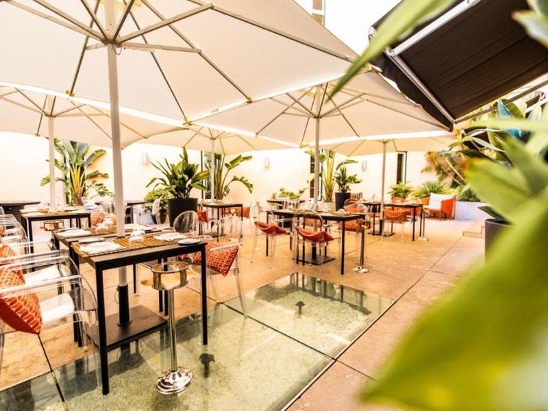 Area pranzo esterna luminosa e moderna con tavoli e sedie eleganti sotto grandi ombrelloni.