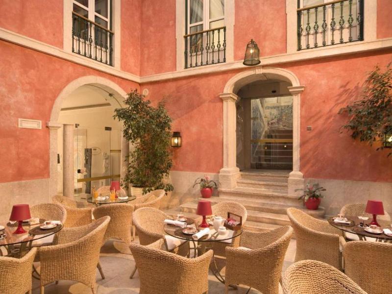 Cortile accogliente con tavoli apparecchiati e sedie davanti a un edificio rosa.