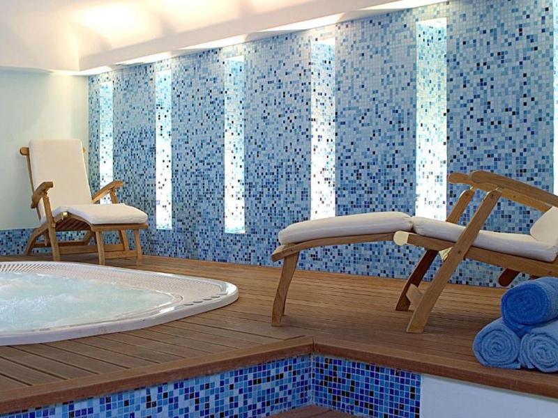 Area interna con vasca idromassaggio, piastrelle a mosaico blu, lettini in legno e asciugamani blu arrotolati.