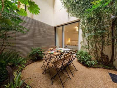 Piccolo cortile con tavolo da giardino e sedie circondato da piante e rampicanti.