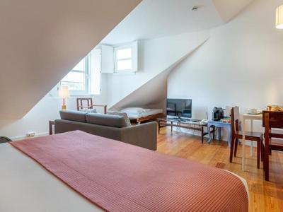 Helle Mansardenwohnung mit Holzboden, grauem Sofa, Fernseher und Esstisch mit vier Stühlen.