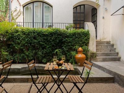 Gemütlicher Außenbereich mit Tischen, Stühlen und Grün entlang einer weißen Fassade.