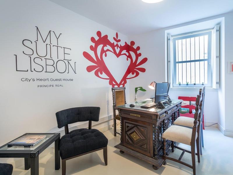 Area reception luminosa con scrivania in legno antico, sedie e decorazione murale in un hotel a Lisbona