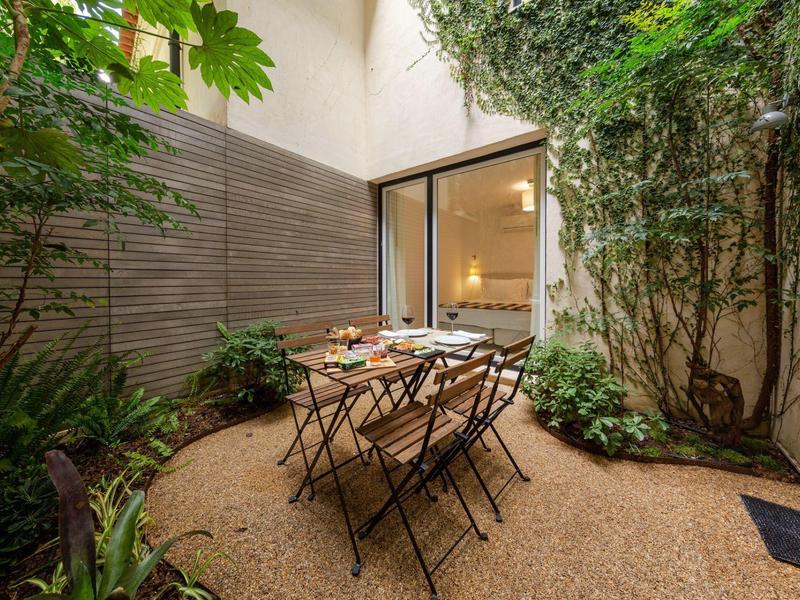 Piccolo cortile con tavolo da giardino e sedie circondato da piante e rampicanti.