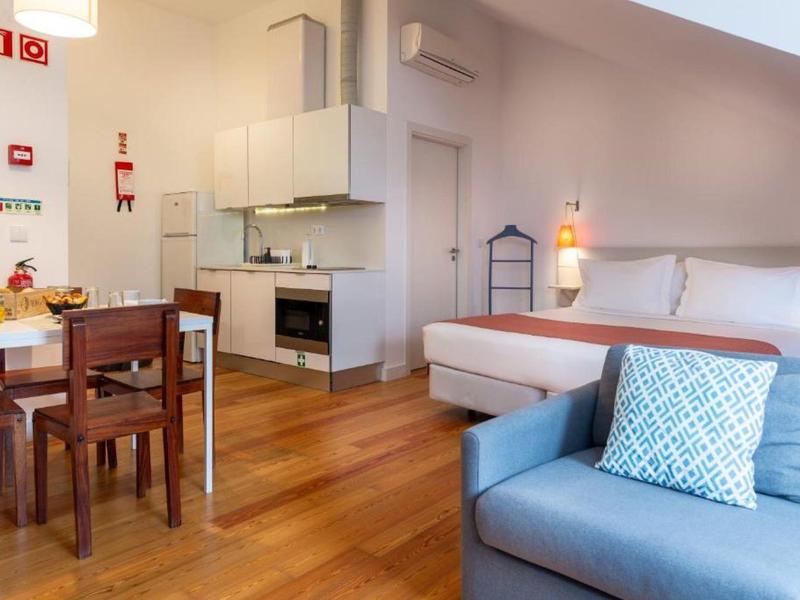 Camera d'hotel moderna con pavimento in legno, letto matrimoniale, tavolo da pranzo e divano con cuscino.