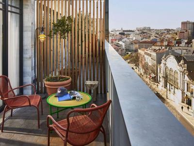 Kleiner Balkon mit zwei roten Stühlen, grünem Tisch und Pflanzen, Blick auf Stadt und Gebäude.