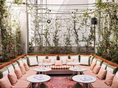 Gezellige buitenlounge met veel roze kussens en kleine ronde tafels in de tuin.