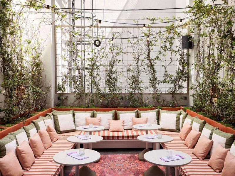 Lounge accogliente con divano ad angolo, cuscini rosa e piccoli tavoli circondati da piante.