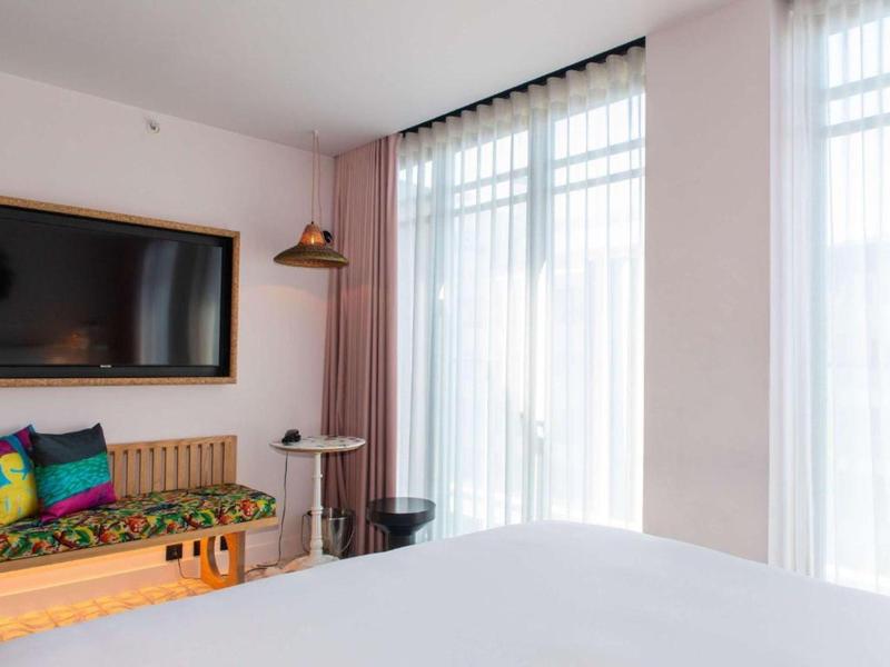 Camera d'hotel luminosa con grande letto, divano colorato e grande finestra con tende.