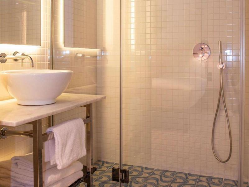 Bagno moderno in hotel con lavabo, doccia in vetro e pavimento decorato.