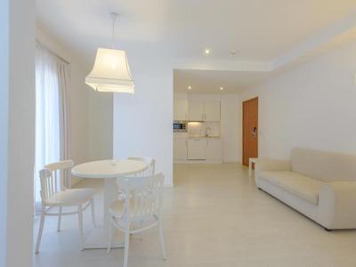 Soggiorno luminoso con tavolo bianco, sedie e divano vicino alla cucina.