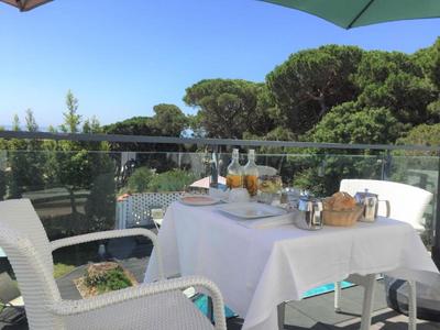 Un tavolo con tovaglia bianca su una terrazza con vista su alberi e piscina.