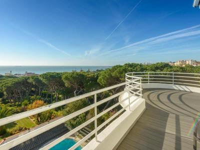 Balcone con ringhiera bianca con vista sul mare e alberi verdi sotto un cielo azzurro.