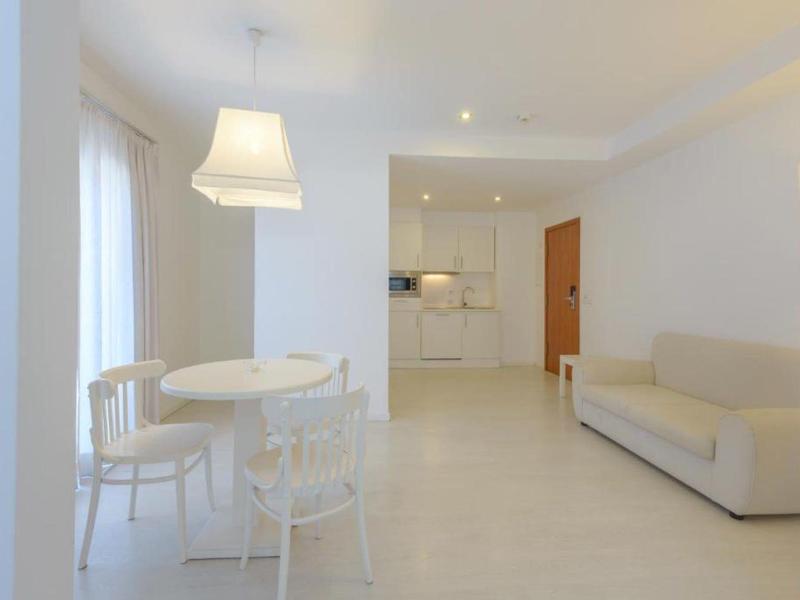 Heller, moderner Wohnraum mit weißem Sofa, runden Tisch, Stühlen und offener Küchenzeile.