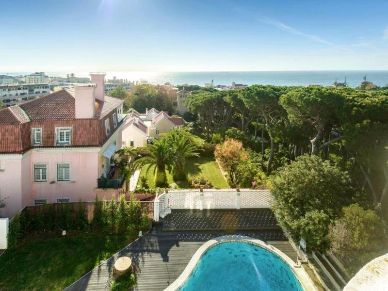 Blick auf ein rundes Schwimmbecken, umgeben von Bäumen und Häusern unter blauem Himmel.