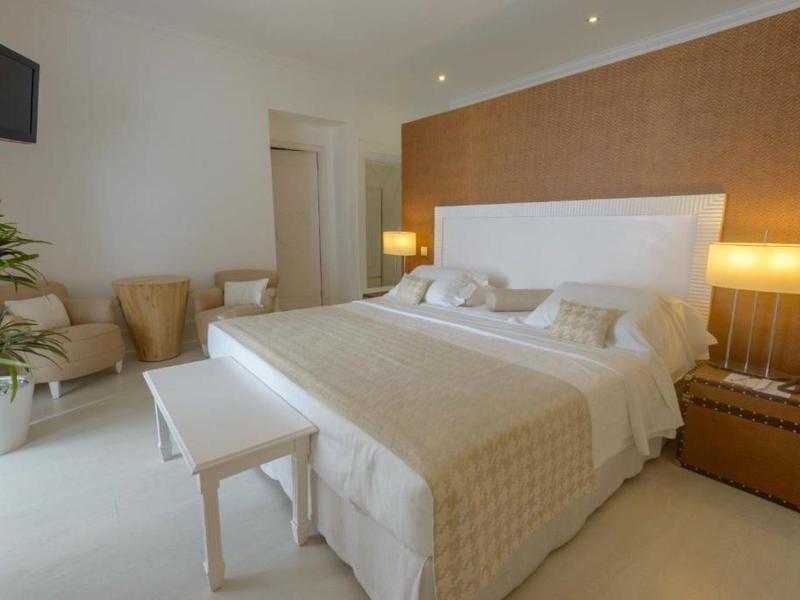 Helles Schlafzimmer mit großem Bett, Nachttischlampen, zwei Sesseln und einer Zimmerpflanze.