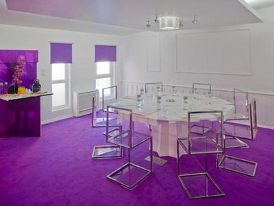 Sala de conferencias moderna con alfombra morada y sillas transparentes alrededor de una mesa redonda