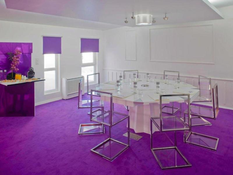 Sala conferenze moderna con moquette viola e tavolo rotondo con sedie trasparenti.