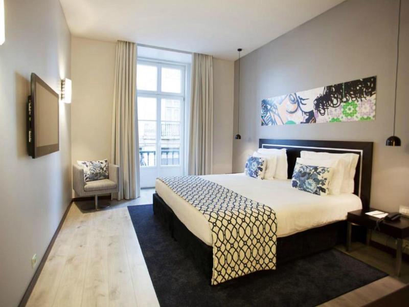 Camera d'hotel luminosa con letto matrimoniale, TV a schermo piatto e finestra con balcone e tende.