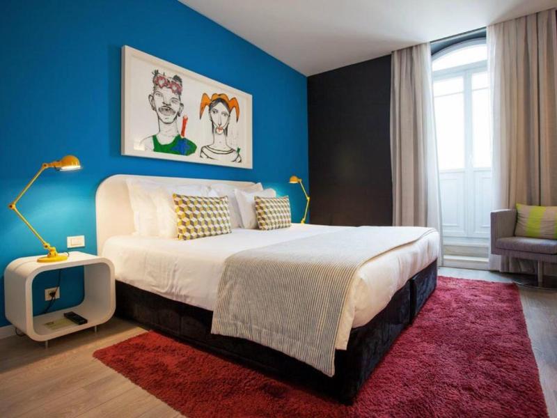 Camera d'hotel moderna con parete blu, letto bianco, arte colorata e tappeto rosso.