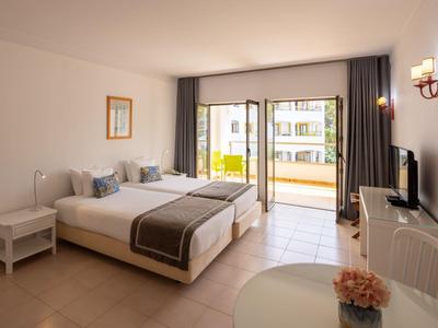 Camera d'hotel luminosa con due letti, balcone e arredi moderni.