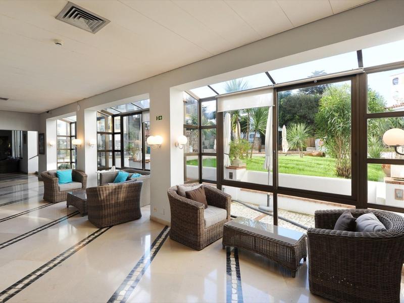 Světý hotelový salon s proutěným nábytkem a výhledem na zahradu