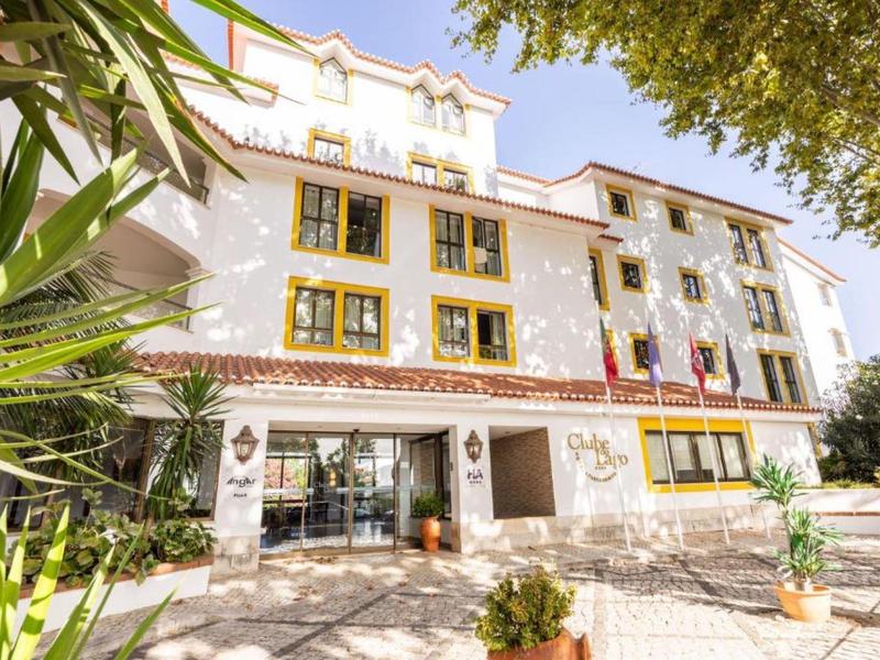 Světlá vícepatrová budova hotelu s velkými okny a upravenými venkovními prostory.