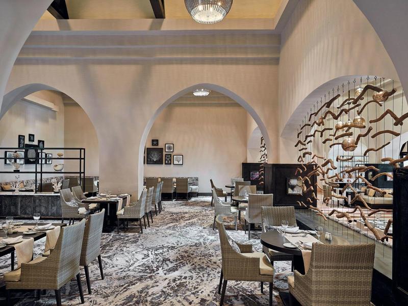 Interior moderno de restaurante con arcos, muebles elegantes y decoración rústica en la pared.