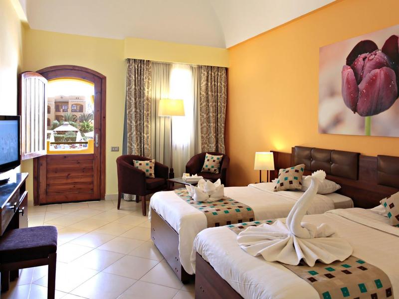 Habitación de hotel luminosa con dos camas individuales, toallas decorativas y tonos cálidos.