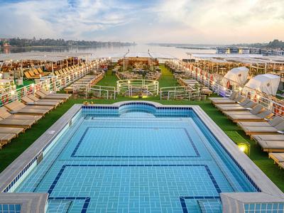 Grande piscine de bateau de croisière entourée de chaises longues et parasols au coucher du soleil.