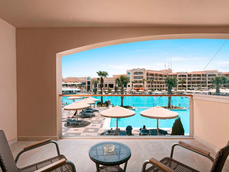 Terrazza con vista su piscina, ombrelloni e hotel sullo sfondo.