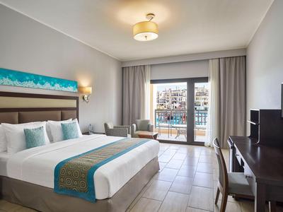 Habitación de hotel moderna con cama grande, área de estar y balcón con vista a la ciudad.