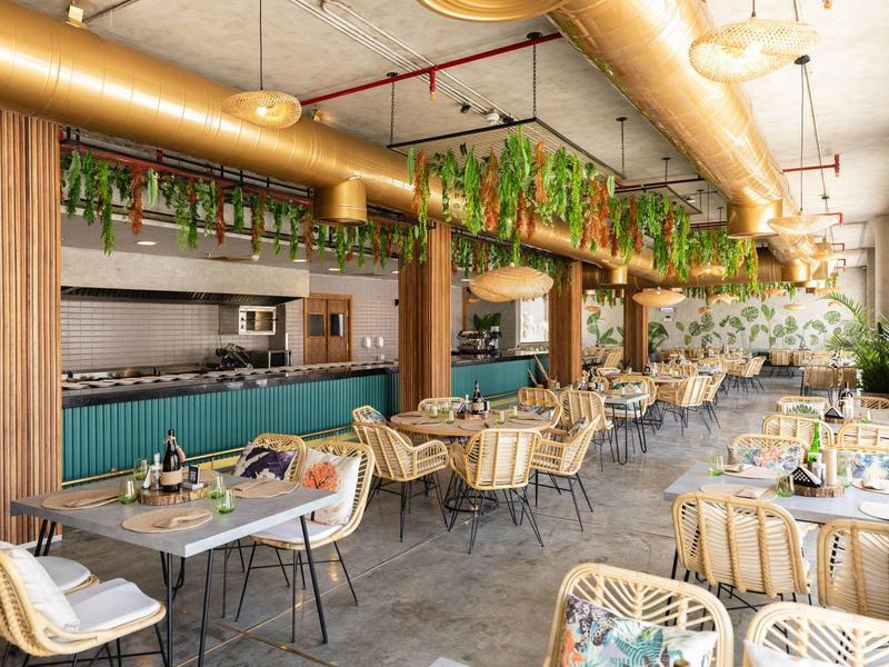 Nowoczesna sala restauracyjna z drewnianymi stolikami, pasiastymi krzesłami i wiszącymi roślinami.