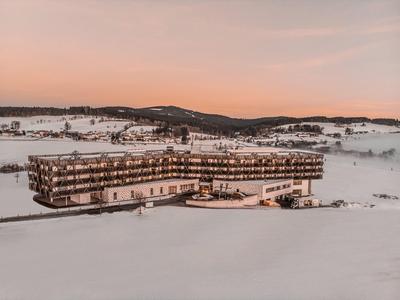 Modernes Hotel mit Panoramafenstern in verschneiter Winterlandschaft bei Sonnenuntergang.