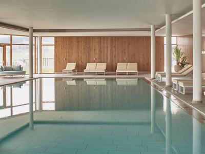 Innenbereich mit großem Schwimmbecken, Holzverkleidung und mehreren weißen Liegestühlen.