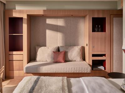 Schlafzimmer mit eingebautem hellholzigen Wandbett, zwei Kissen, großem Bett und weicher Tagesdecke.