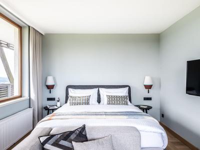 Modernes Schlafzimmer mit grauen Wänden, großem Bett, grauem Sofa und Fernseher an der Wand.