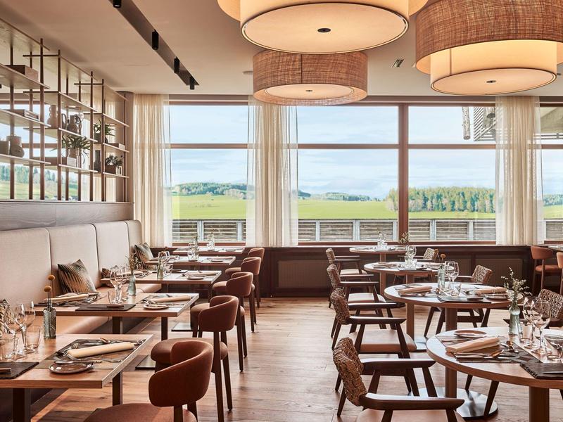 Modernes Restaurant mit Holzboden, braunen Stühlen, großen Fenstern und runden Lampen an der Decke.