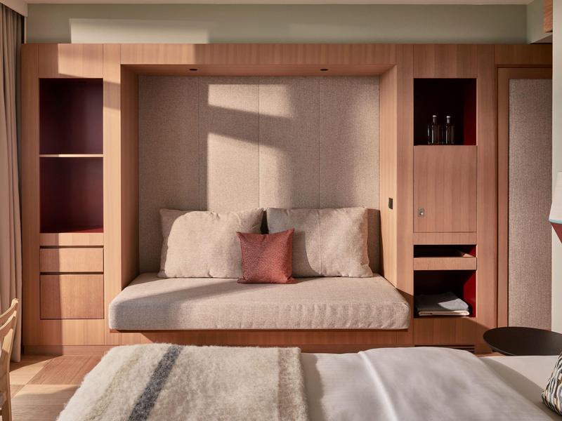 Schlafzimmer mit eingebautem hellholzigen Wandbett, zwei Kissen, großem Bett und weicher Tagesdecke.