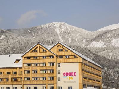 Großes Hotelgebäude aus Holz in verschneiter Berglandschaft bei klarem Himmel.