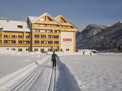 Skifahrer auf Loipe vor großem Hotel im verschneiten Bergtal bei klarem Himmel