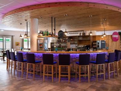 Moderne Hotelbar mit rundem Holztresen und bequemen Hockern in lila Polsterung.