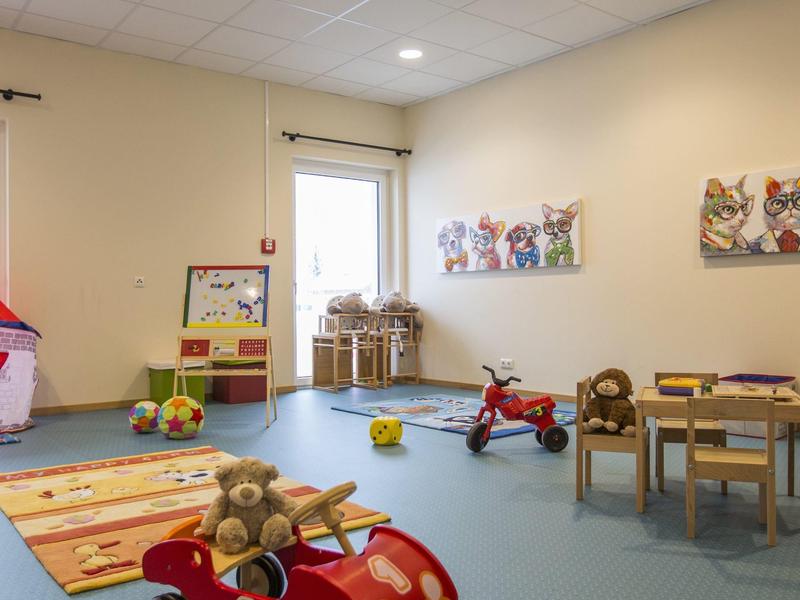 Kinderspielzimmer mit Spielzeugauto, Tisch, Stühlen und bunten Wandbildern.