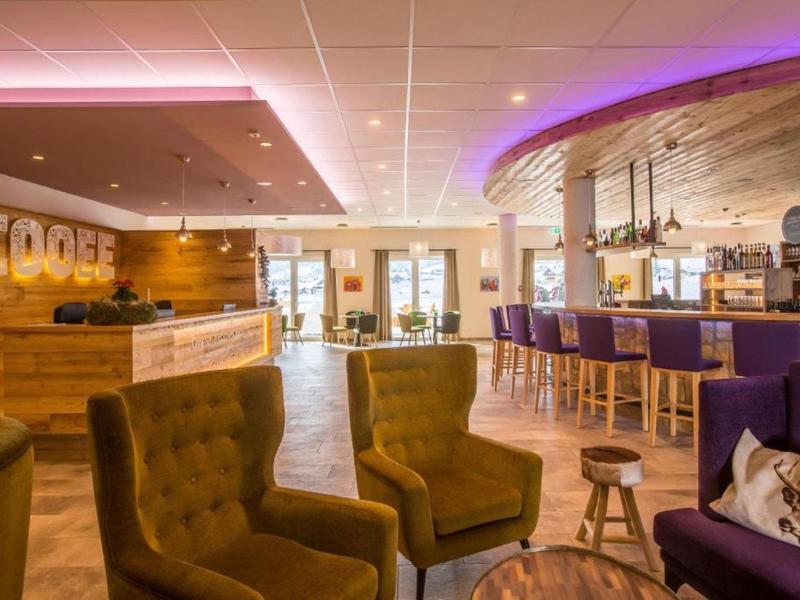 Moderne Café-Lounge mit Holzvertäfelung, bequemen Sesseln und eleganter Bar mit violetten Akzenten.