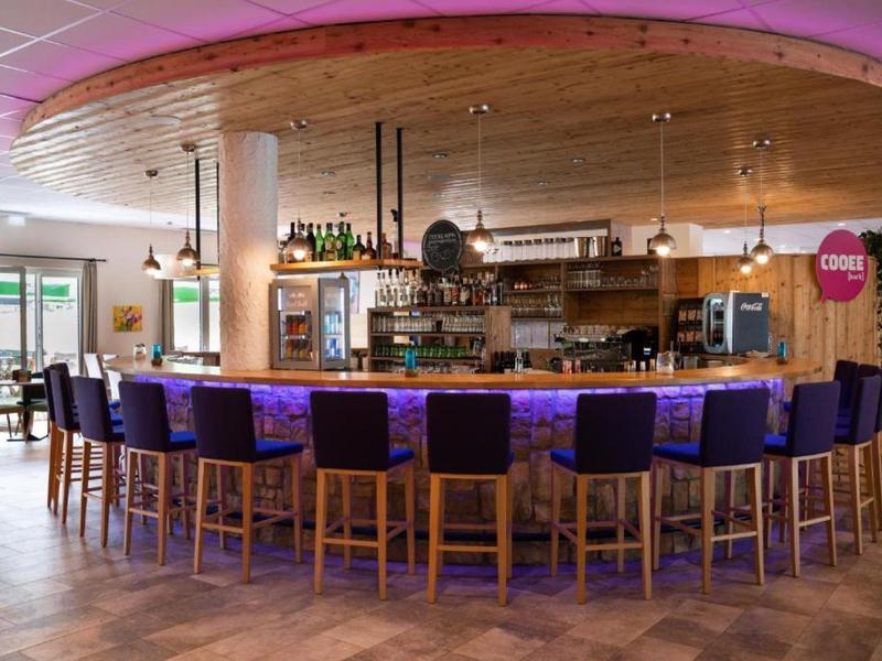 Moderner Barbereich mit rundem Holztresen, violetten Barhockern und Deckenbeleuchtung.